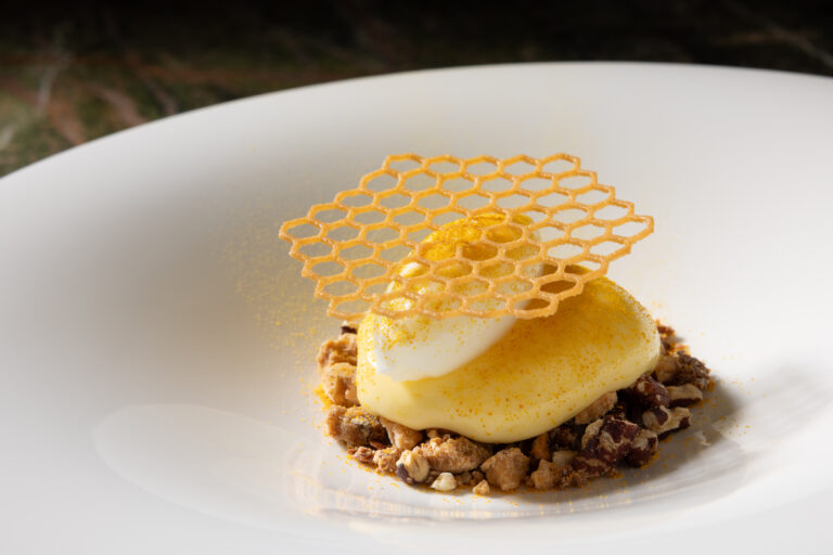 Dessert mit cremiger Nocke, knusprigem Wabengebäck und Nuss-Crumble auf einem weißen Teller.